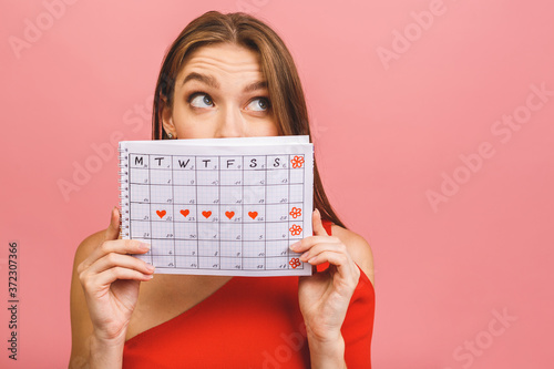 Cuadros en Lienzo Portrait of a funny young girl hiding behind a periods calendar isolated over pink background