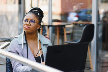 Human and technology. Young african woman typing on laptop, texting friends via social networks. Student girl browsing Internet, using free wi-fi, sitting at cafe near window on sunny day