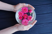 Hands Holding A Round Glass Vase With Buds Of Red Roses Of Black Table