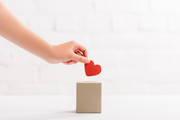Wall Mural - cropped view of female hand putting red heart in box on white background, donation concept