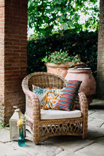 Flowers Inglass Vase And Antique Lantern Close To Wicker Chair With Decorated Cushions Under Patio
