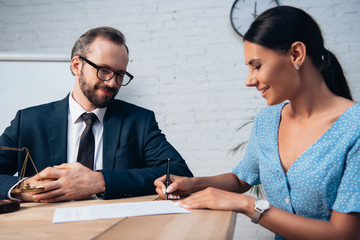 selective focus of bearded lawyer in glasses looking at woman signing insurance contract in office