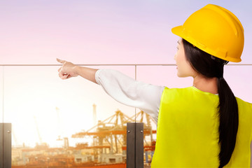 Rear view of an Asian construction worker with hardhat pointing at the seaport