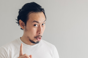 Funny grinning smile face of Asian man in white t-shirt and grey background.