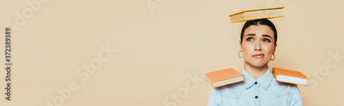 Fotografía skeptical student in denim shirt with books on head and shoulders isolated on be