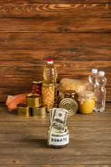 Wall Mural - selective focus of jar with money and donated food on wooden background, charity concept
