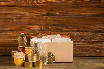 Wall Mural - cardboard box with groats near water, oil, canned food and honey on wooden background, charity concept