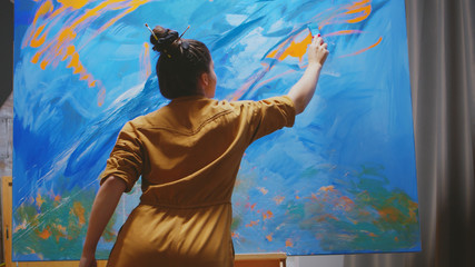 Wall Mural - Innovative female painter using orange paint on big canvas.