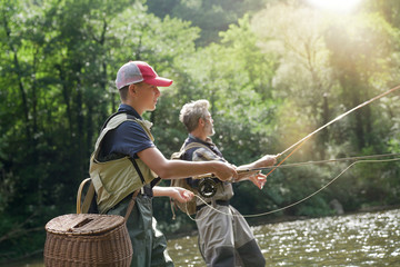 a father and his son fly fishing in summer on a beautiful trout river with clear water