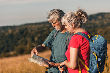 Wall Mural - Active senior couple hiking in nature with backpacks, enjoying their adventure at sunset.