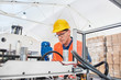 © Karanov images - Portrait of a worker in a factory wearing reflective vest and safety helmet, adjusting the machine