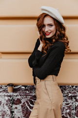 Wall Mural - Beautiful european woman in brown beret enjoying good day. Wonderful french female model with ginger hair posing outdoor.