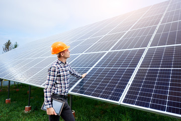 Wall Mural - Male engineer in a helmet with a tablet in his hands standing near the solar panels, looking up. Green ecological power energy generation. Solar station development concept. Home construction.