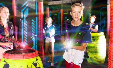 Portrait of teenager boy with laser gun having fun on dark lasertag arena..