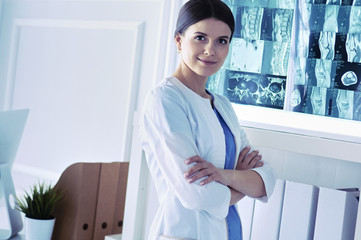 Portrait of young female doctor in white coat standing in hospital with her hands crossed