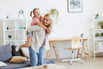 Mother riding her daughter with down syndrome on her back while they playing in the living room