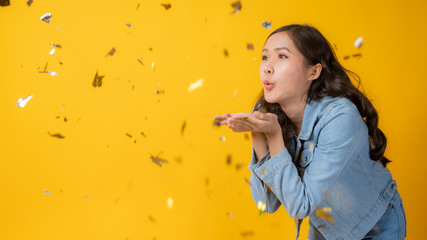 Asian beautiful woman blowing and celebrate, Cute Thai girl blow paper for celebration in studio on yellow background