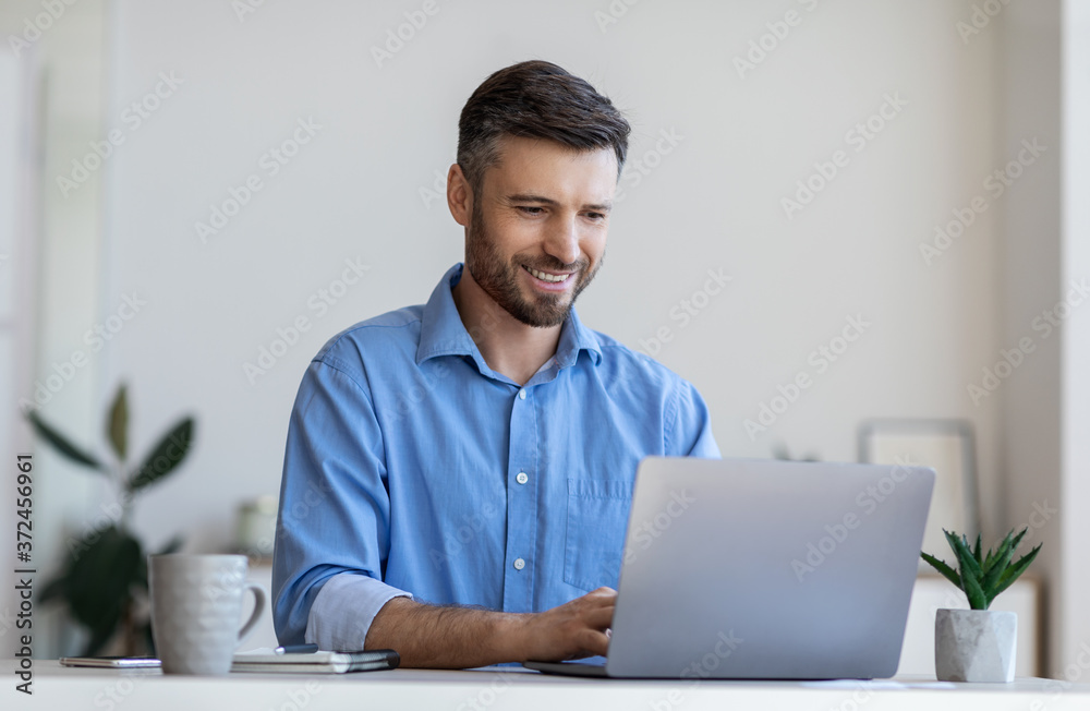 Handsome male entrepreneur working on laptop at desk in modern office - obrazy, fototapety, plakaty 