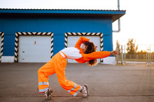 Young African American Woman - Dancer Dancing In The Street At Sunset. Stylish Woman With Curly Hair In An Orange Suit  Showing Some Moves. Sport, Dancing And Urban Culture Concept.