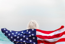 Caucasian Blonde Woman Holding American Flag Leaning Against Back And Looking At Sea