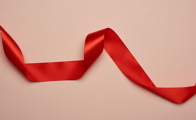 Poster - twisted red silk ribbon on a beige background