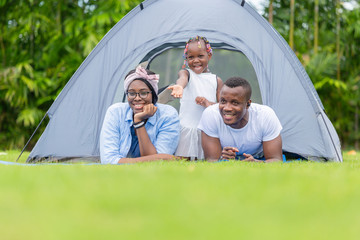 cheerful african american family enjoying in the park, mother father and daughter playing camping at