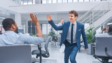Poster - Young Happy Business Manager Wearing a Suit and Tie Dancing and Giving High Fives in the Office. Celebrating Success. Diverse and Motivated Business People Work on Computers in Modern Open Office.