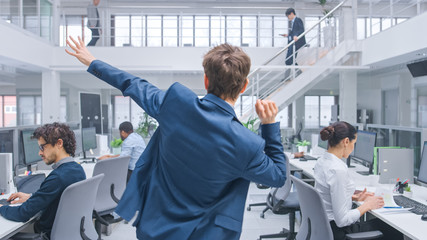 Poster - Back View Shot of a Young Cheerful Handsome Business Manager Wearing a Suit and Tie Dancing in the Office. Diverse and Motivated Business People Work on Computers in Modern Open Office.