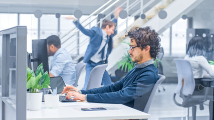 Poster - Young Handsome Manager with Curly Hair Works on a Desktop Computer and Compares Data with a Software. Diverse and Motivated Business People Work on Computers in Modern Open Office.