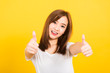 Asian happy portrait beautiful cute young woman teen standing wear t-shirt showing gesturing finger thumb up looking to camera isolated, studio shot on yellow background with copy space