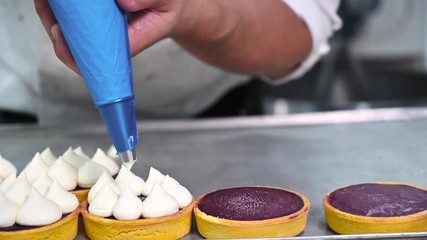 Wall Mural - Pastry chef decorates biscuit tartlet with cream from pastry bag, close-up. Preparation of cake at commercial bakery with piping bag. High quality 4k footage.