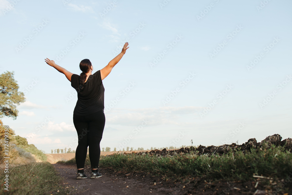 Body positive, freedom, high self esteem, confidence, happiness, inspiration, success, positive affirmation. Overweight woman celebrating rising hands to the sky - obrazy, fototapety, plakaty 