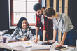 © BullRun - Young crew of male and female designers brainstorming while creating interior outlay discussing ideas about coloristic and space planning pointing on architectural drawings solutions in studio