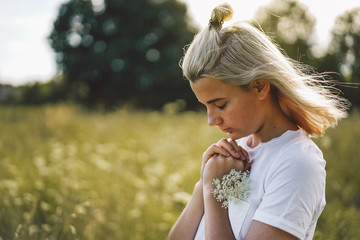 Wall Mural - Girl closed her eyes, praying in a field.  Hands folded in prayer concept for faith