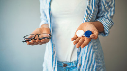 Wall Mural - woman holding plastic container with contact lenses and glasses, closeup. young woman choosing betwe