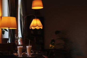 interior in a cafe with lampshades, a table with two glasses of coffee latte  in warm dark colors, there is room for text