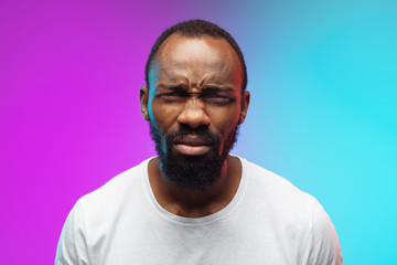 Wall Mural - Close up eyeing. African-american young man's portrait on gradient background in neon. Beautiful male model in casual style, white shirt. Concept of human emotions, facial expression, sales, ad.