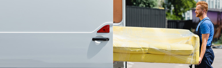 Wall Mural - Horizontal image of loader holding couch near truck with open doors on urban street