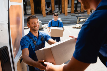 Poster - Selective focus of loader giving carton box to colleague in truck on urban street