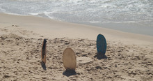 Três Pranchas De Bodyboard Espetadas Na Areia Da Praia Perto Da água Mar Com Um Circulo Desenhado Na Areia, Final Da Tarde, Fato De Neopreno Pendurado Numa Prancha De Bodyboard