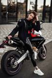 Fototapeta Miasto - Sexy brunette girl in a black motorcycle jacket sits on a purple sport motorbike