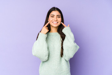 Wall Mural - Young indian woman isolated on purple background smiles, pointing fingers at mouth.