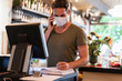 © Daniel Ingold/Westend61 - Restaurant manager with protective mask using computer and smartphone for reservation