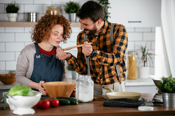 Wall Mural - Boyfriend and girlfriend making delicious food at home. Loving couple cooking in kitchen.