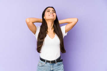 Wall Mural - Young indian woman isolated on purple background feeling confident, with hands behind the head.