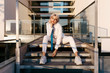 © Tania Cervián/Westend61 - Young woman wearing white suit sitting on steps against modern building