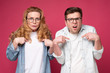 © Viktor Koldunov - Are you talking about us concept. Handsome frowning man and woman pointing fingers at themself, having doubtful confused facial expression. Studio shot