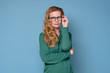 © Viktor Koldunov - Confident mature woman in glasses looking at camera standing against blue background.