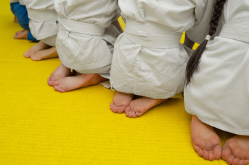 naked legs and heels of children in white tracksuits with wrestling belts on a yellow mattress