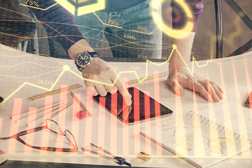 Double exposure of man's hands holding and using a digital device and forex graph drawing. Financial market concept.